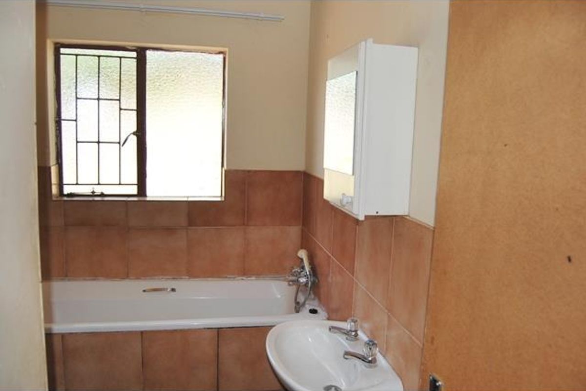 A functional bathroom featuring a standard bathtub, wall-mounted basin, and a medicine cabinet, finished with dated brown wall tiling.
