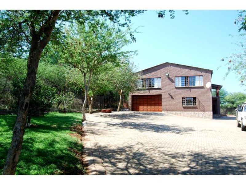 Front view of a brick farmhouse featuring a paved driveway, integrated garage, and established garden surroundings.