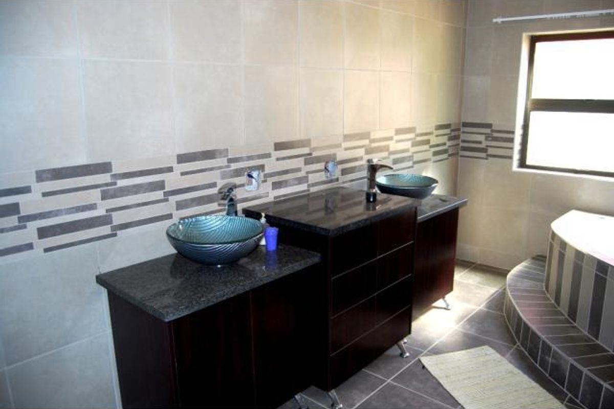 A modern bathroom featuring a double vanity with granite countertops, vessel sinks, and tiled wall finishes with a built-in bathtub.