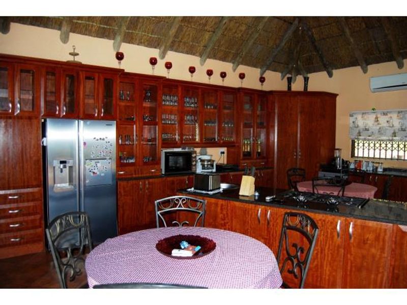 Spacious kitchen featuring extensive wooden cabinetry, granite countertops, integrated appliances, and a traditional thatch ceiling, offering a warm and rustic aesthetic.