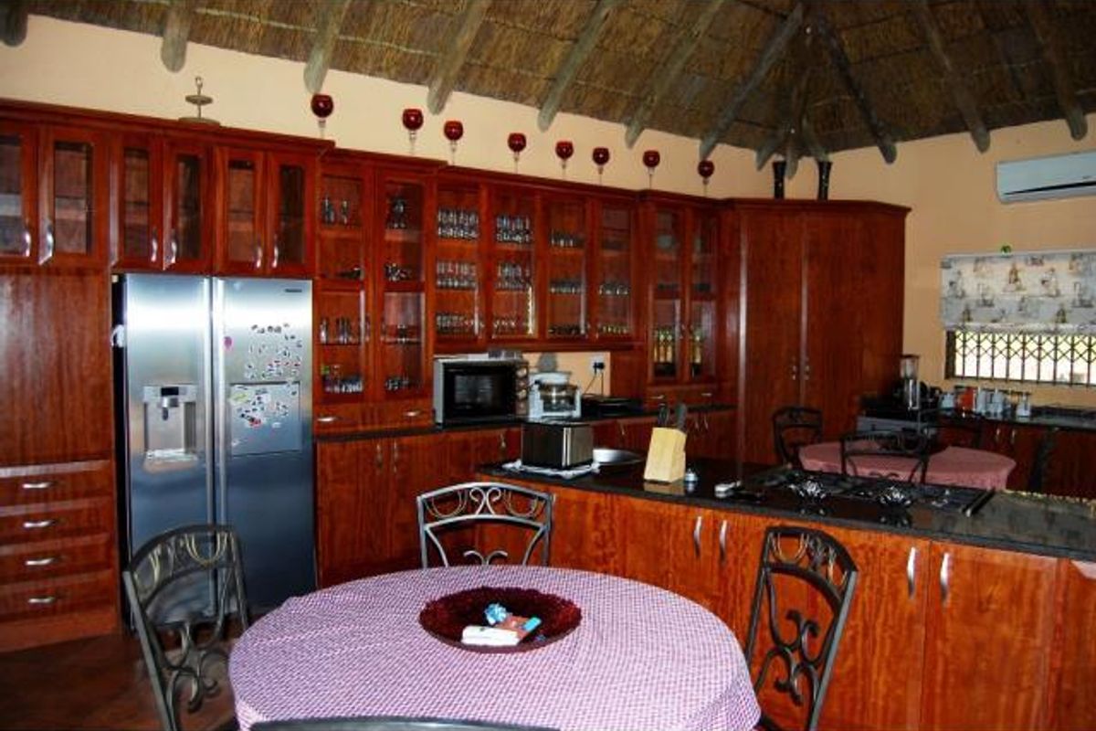 Spacious kitchen featuring extensive wooden cabinetry, granite countertops, integrated appliances, and a traditional thatch ceiling, offering a warm and rustic aesthetic.