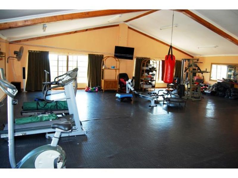 Spacious home gym featuring vaulted ceilings with exposed timber beams and durable rubberized flooring, providing a functional workout environment.