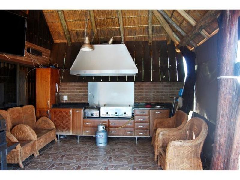 Covered outdoor patio area featuring a built-in braai, stainless steel extractor hood, wooden cabinetry, and rustic thatched roof detailing.