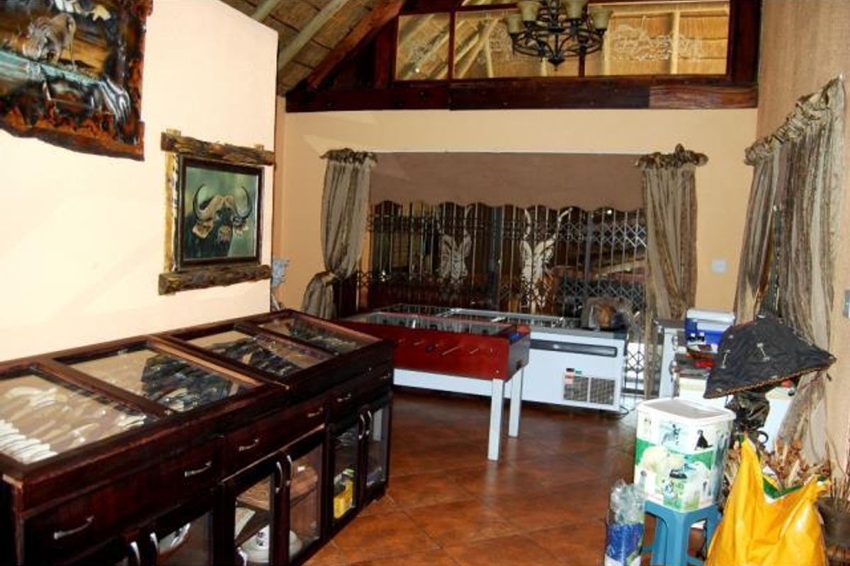 Spacious living area featuring a high thatched ceiling with exposed timber beams, tiled flooring, and a large security gate leading to the exterior.