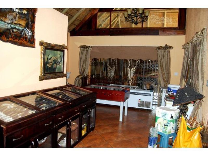 Spacious living area featuring a high thatched ceiling with exposed timber beams, tiled flooring, and a large security gate leading to the exterior.
