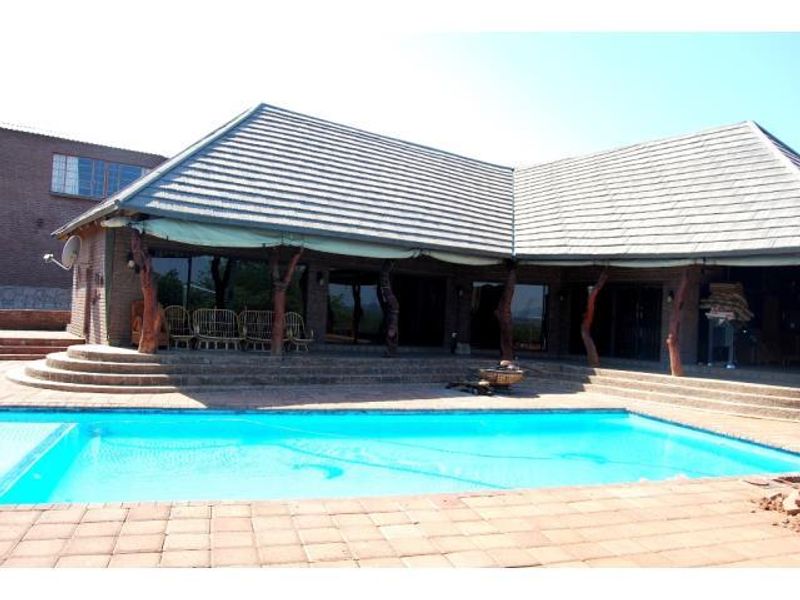 Outdoor pool area featuring a swimming pool, paved patio, and covered veranda with brick pillars and sliding glass doors.