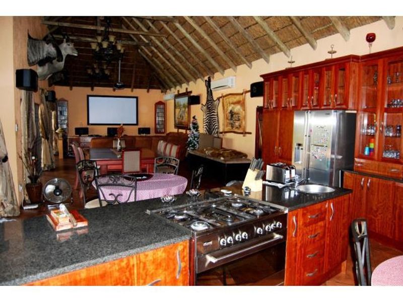 Spacious open-plan living and kitchen area featuring a high vaulted thatch ceiling with exposed timber rafters and custom wooden cabinetry.
