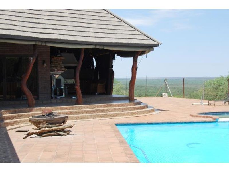 Outdoor entertainment area featuring a swimming pool, spacious tiled patio, and a covered veranda with a built-in braai overlooking the landscape.