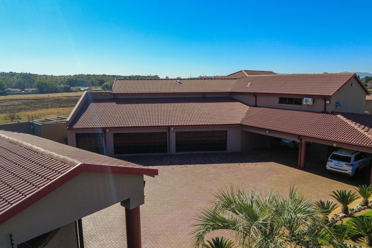 Aerial view of the property featuring a large paved driveway, multiple garage doors, and a tiled roof structure.