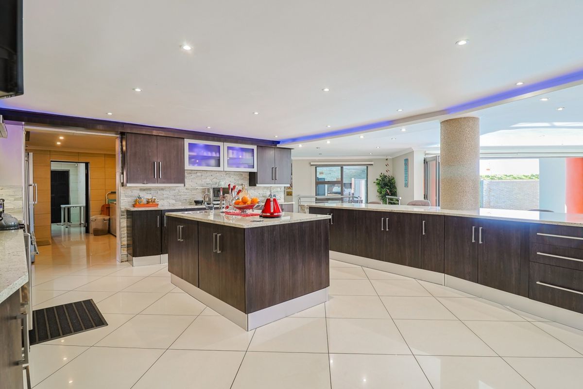 Modern open-plan kitchen featuring dark wood cabinetry, stone countertops, a central island, and recessed ceiling lighting with integrated ambient LED accents.