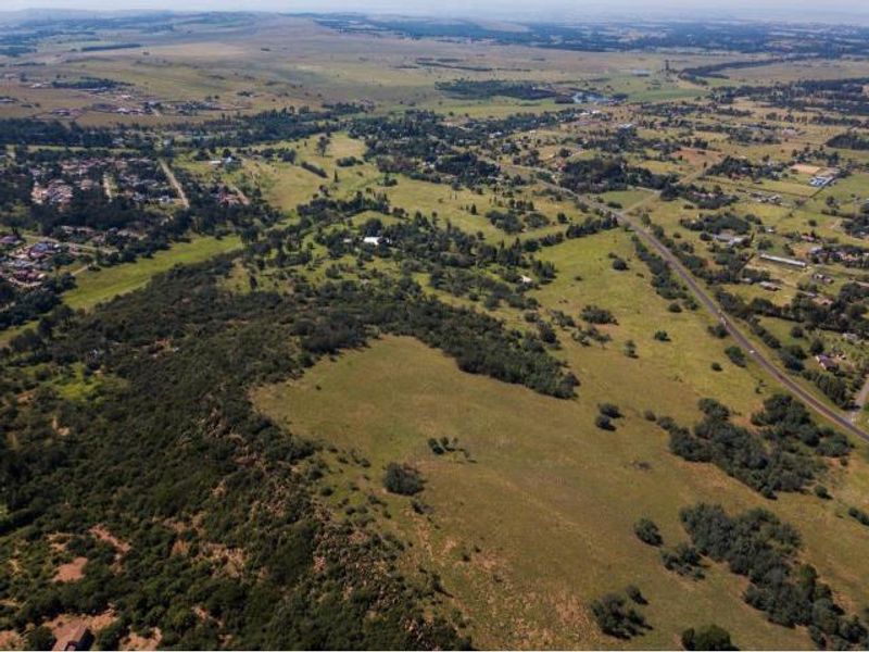 An expansive aerial view of the vacant residential land, showcasing the surrounding landscape, natural vegetation, and proximity to local infrastructure and roads.