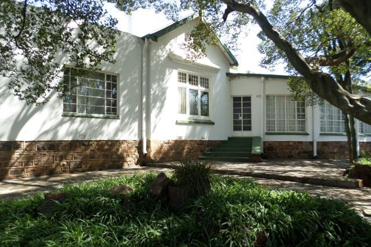 A view of the rear exterior facade featuring stone base detailing, multi-pane windows, and a paved patio area surrounded by mature trees.