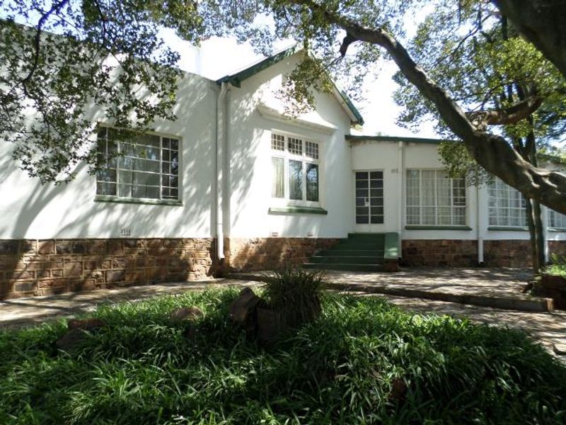 A view of the rear exterior facade featuring stone base detailing, multi-pane windows, and a paved patio area surrounded by mature trees.