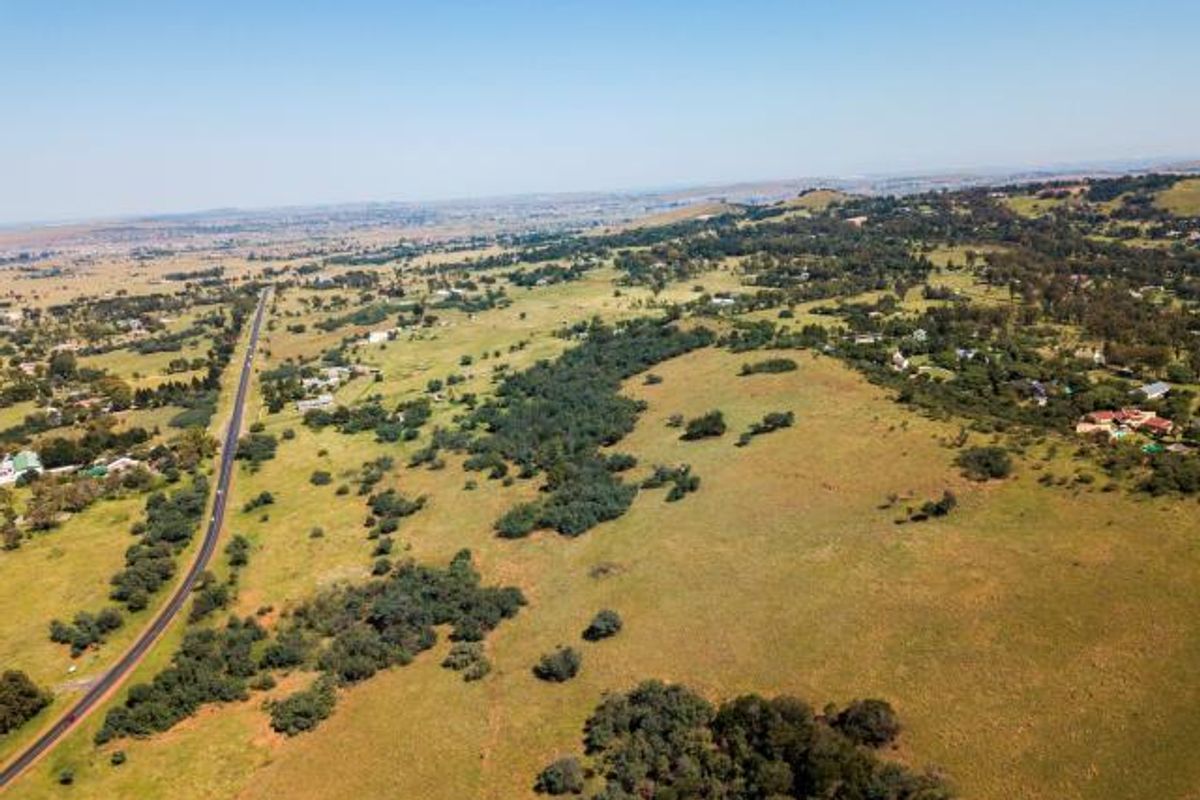 An aerial view of a large, undeveloped residential land parcel featuring rolling grassy terrain, scattered trees, and proximity to a main road.