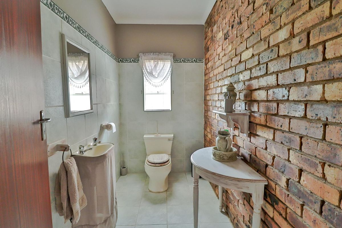 A bathroom featuring a rustic exposed brick wall, ceramic tiling, a pedestal basin, and a standard toilet.
