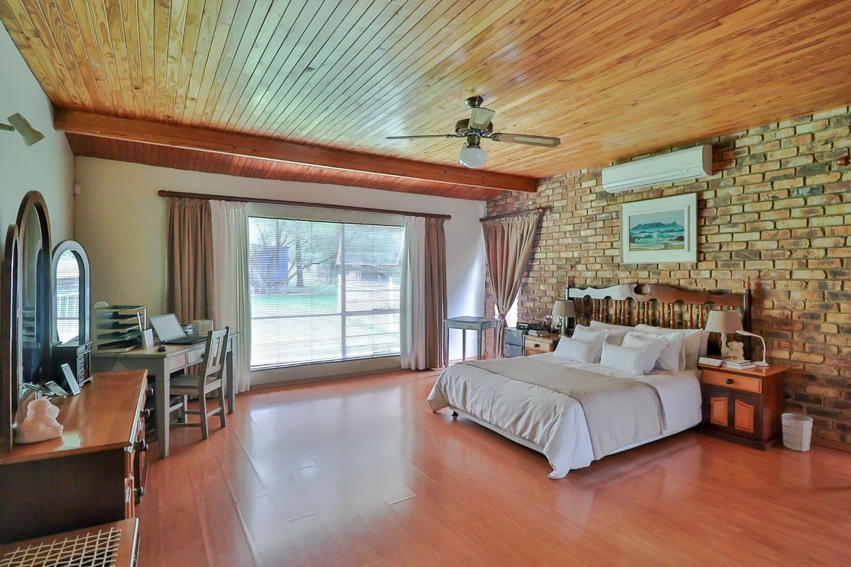 Spacious bedroom featuring a warm timber ceiling, exposed brick feature wall, laminate flooring, and a split-system air conditioner for climate control.