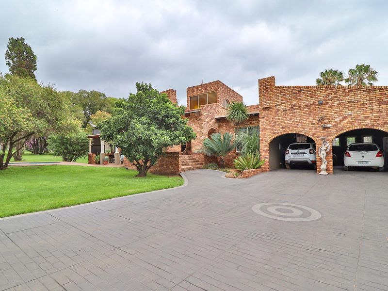 A well-maintained face-brick small holding property featuring a spacious paved driveway, double garage, and established garden surroundings.