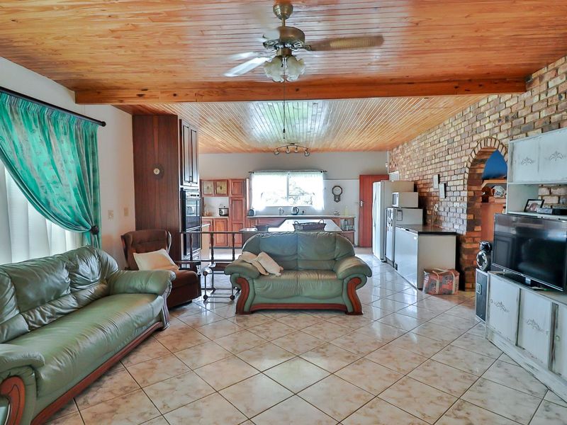 Spacious open-plan living and kitchen area featuring an exposed timber ceiling, brick feature wall, and tiled flooring throughout.