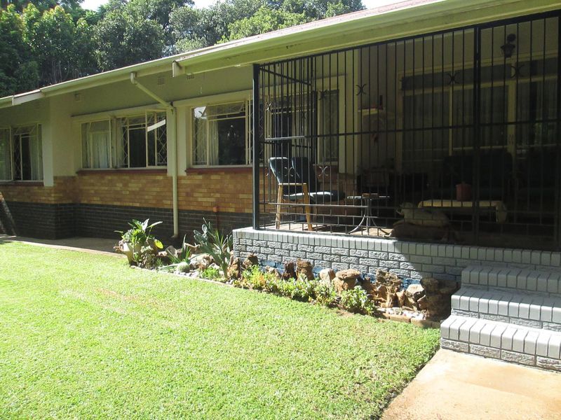 A rear view of the house featuring a covered patio area with security gates, brick facade, and a well-maintained lawn.