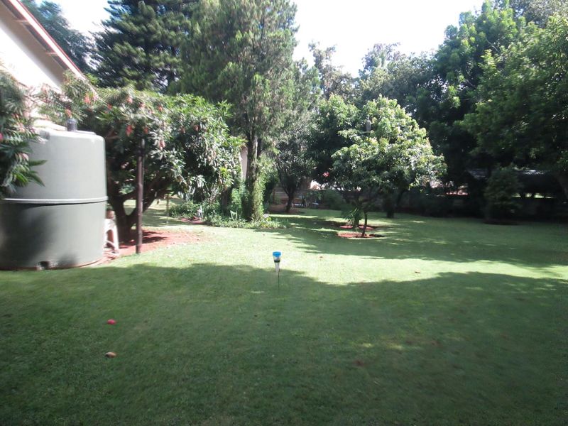 A spacious, well-maintained private garden featuring mature trees, lush lawn, and a large integrated water storage tank.
