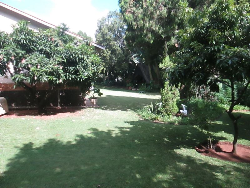 A lush, well-established garden area featuring mature trees, manicured lawn, and partial view of the property's exterior side elevation.