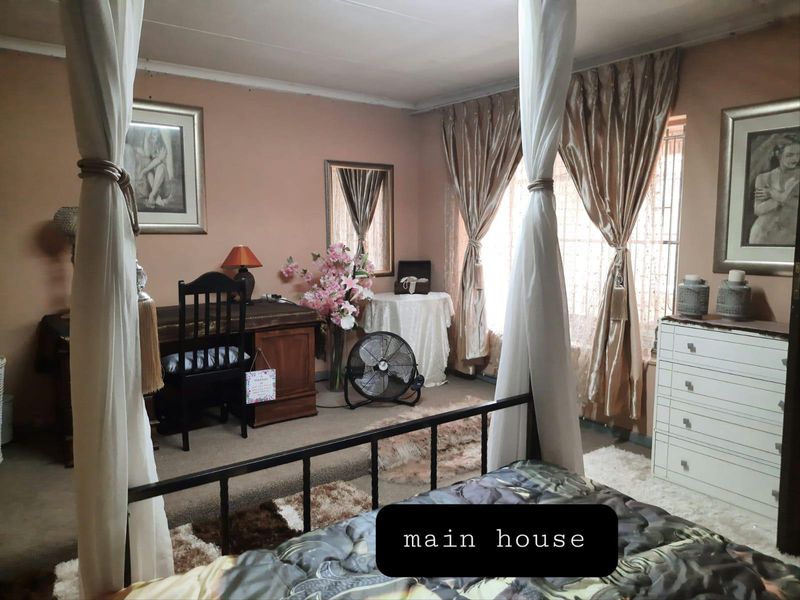 A bedroom featuring neutral wall tones, window security bars, and curtain rails, providing a functional space within the main house.