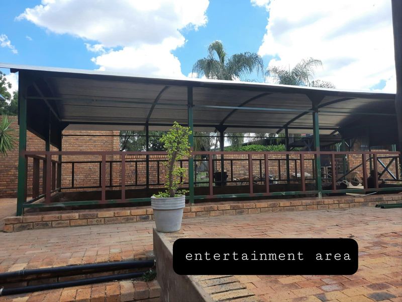Covered outdoor entertainment area featuring a metal roof structure, brick paving, and perimeter metal railings, suitable for hosting gatherings.
