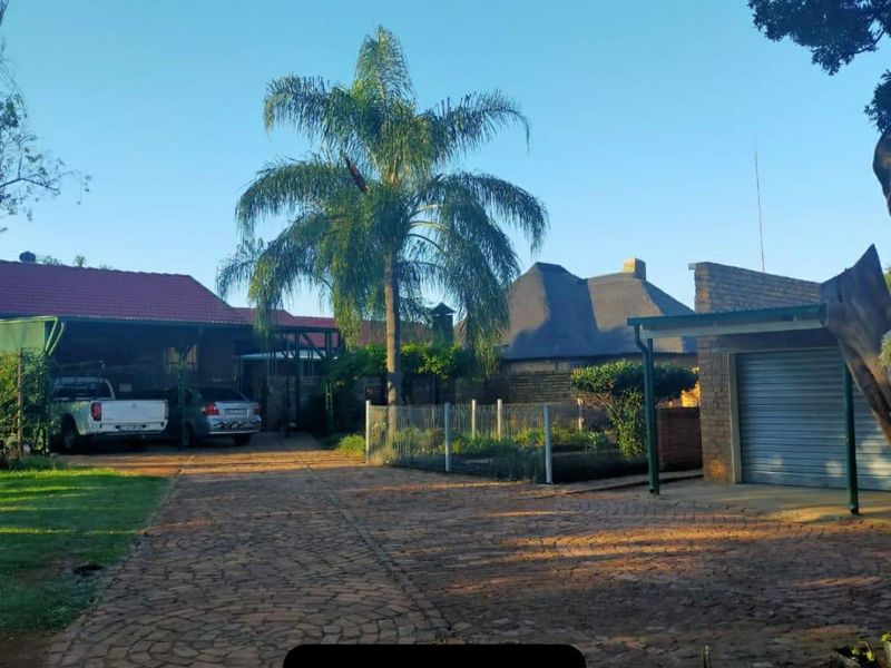Front view of the farm property featuring a paved driveway, carport, garage, and a mix of traditional thatched and metal roofing.