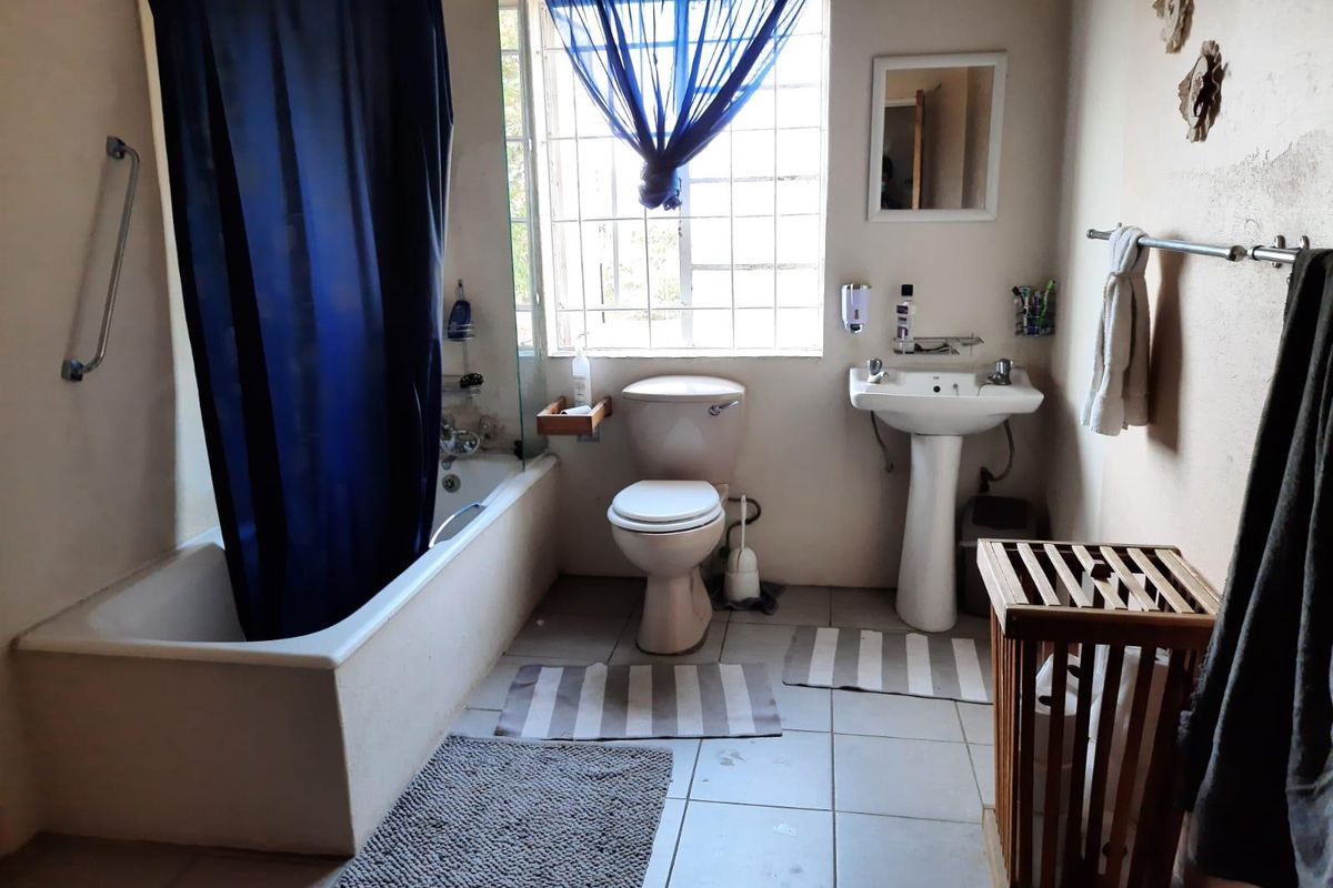A functional bathroom featuring a bathtub, pedestal sink, and toilet, with tiled flooring and a window providing natural light.