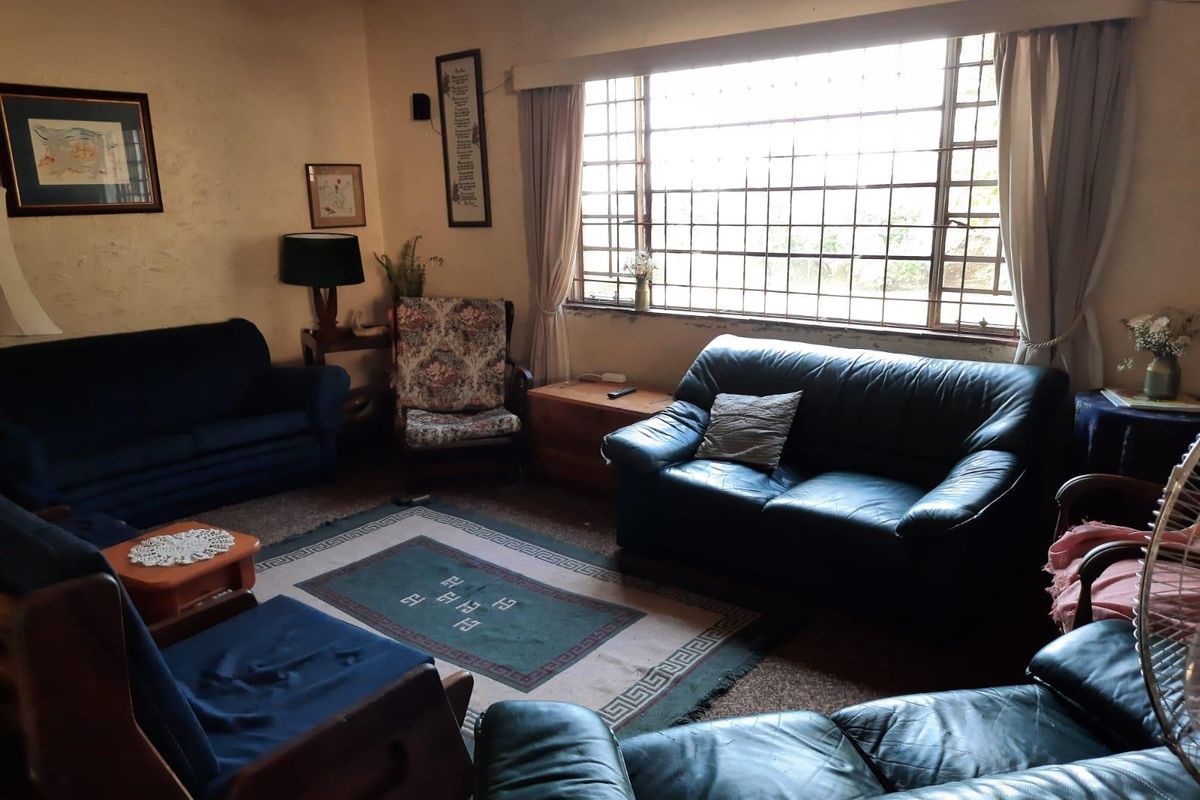 A living room featuring a large window with security bars, providing natural light. The space requires cosmetic updates to the wall finishes.