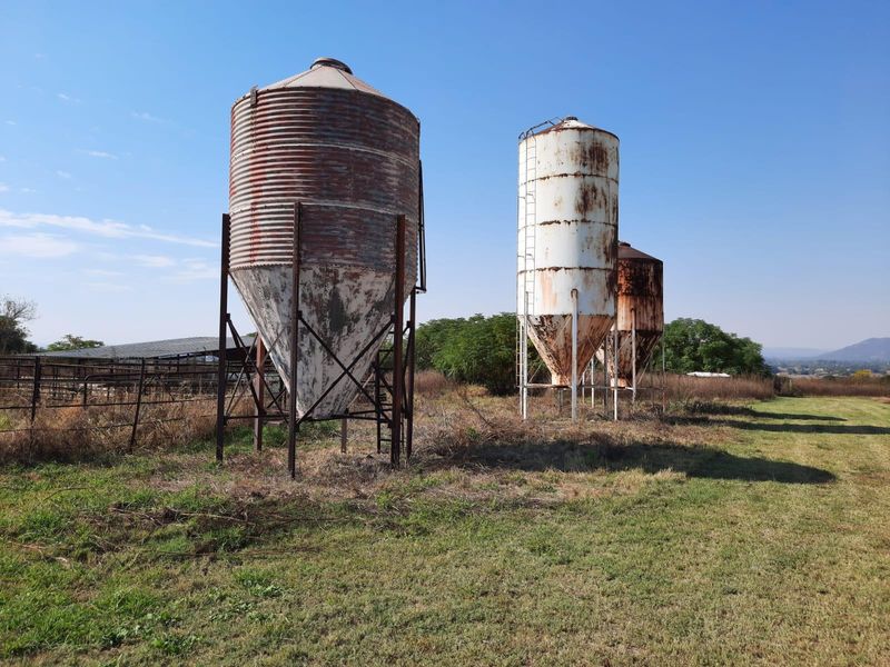 A set of three weathered metal grain silos situated on the farm property, showing signs of age and surface corrosion.