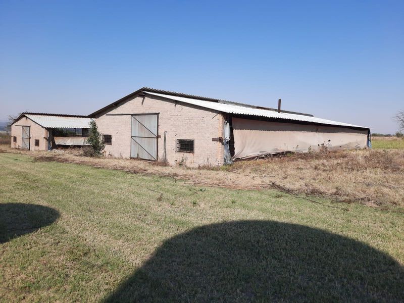 Exterior view of a large farm outbuilding featuring brick masonry construction, corrugated metal roofing, and sliding metal access doors.