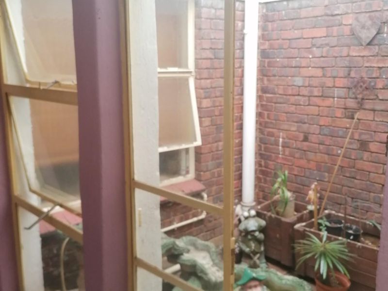 A small enclosed courtyard or patio area featuring exposed brick walls, paved flooring, and access through a screen door.