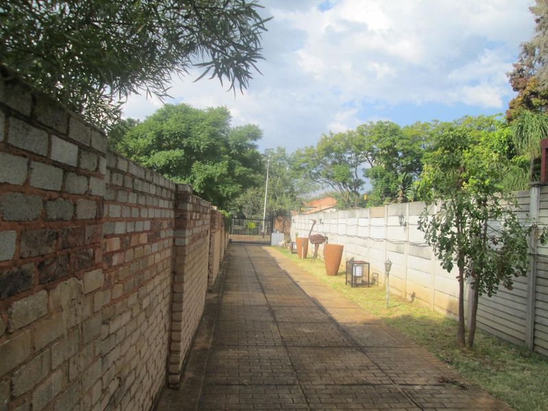 A long paved driveway leading to a secure metal gate, flanked by a brick boundary wall and a precast concrete wall.