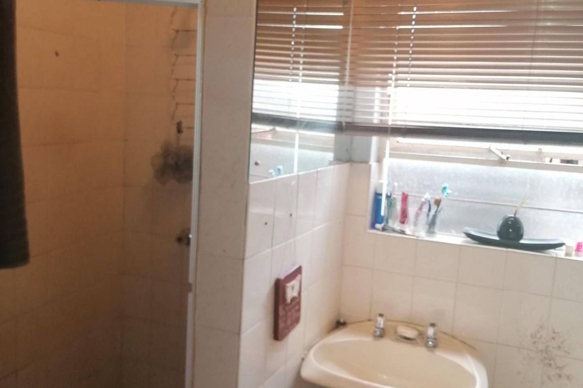 A functional bathroom featuring a pedestal basin, a tiled shower enclosure, and wall-mounted mirror, requiring cosmetic updates to modernize the space.