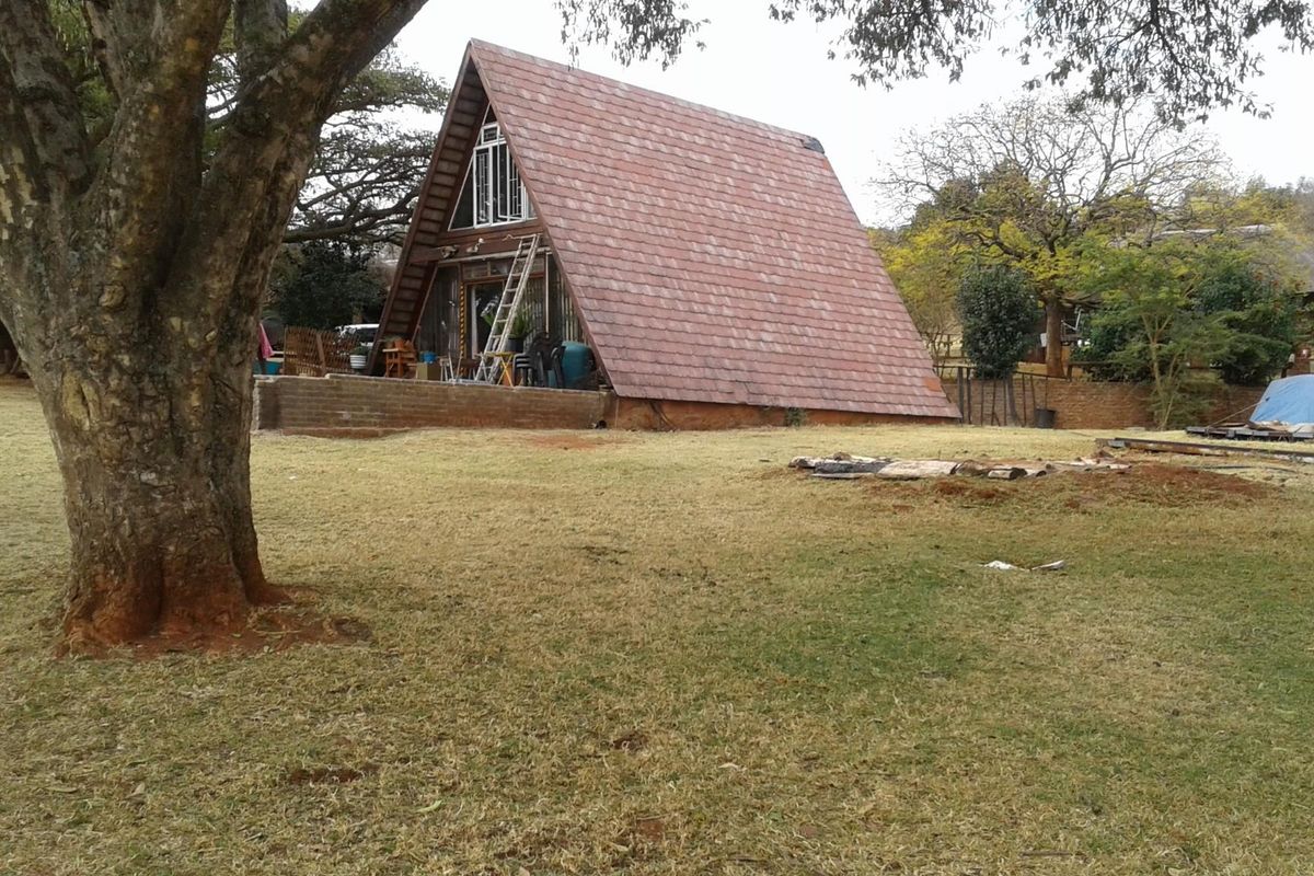 Rear view of an A-frame farm house featuring a tiled roof and an attached brick patio set within a large garden area.