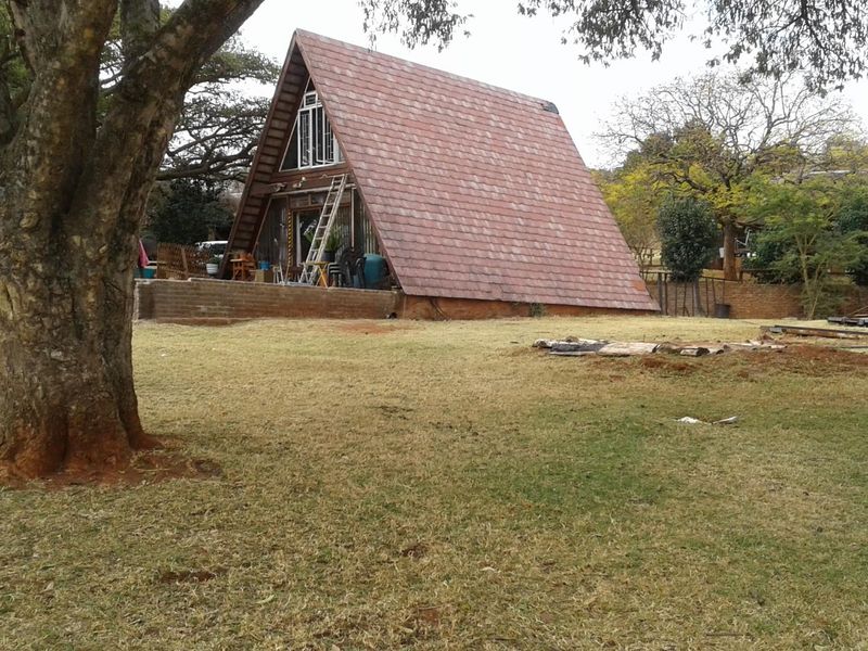 Rear view of an A-frame farm house featuring a tiled roof and an attached brick patio set within a large garden area.