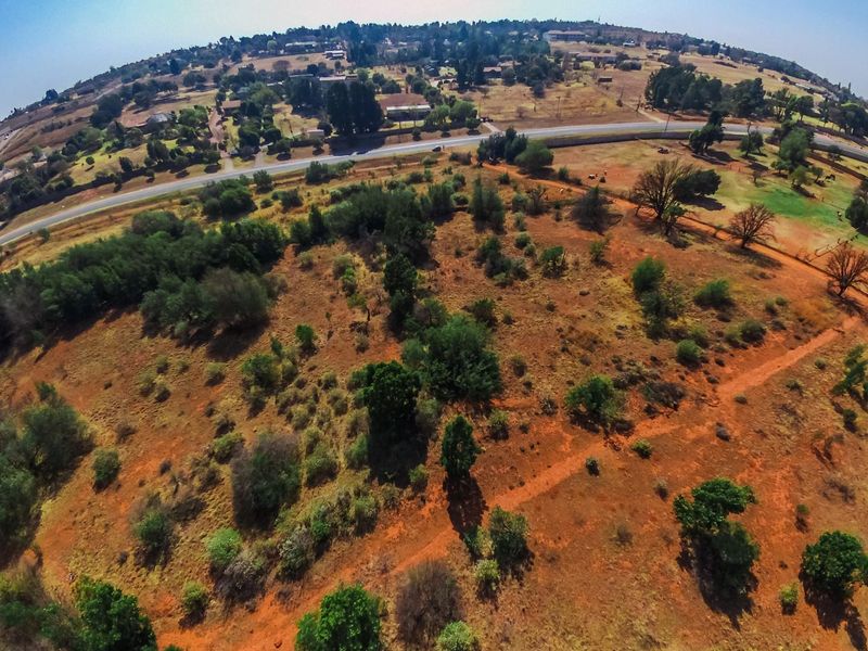 An aerial view of a large, undeveloped farm plot featuring natural vegetation, dirt paths, and surrounding rural landscape.