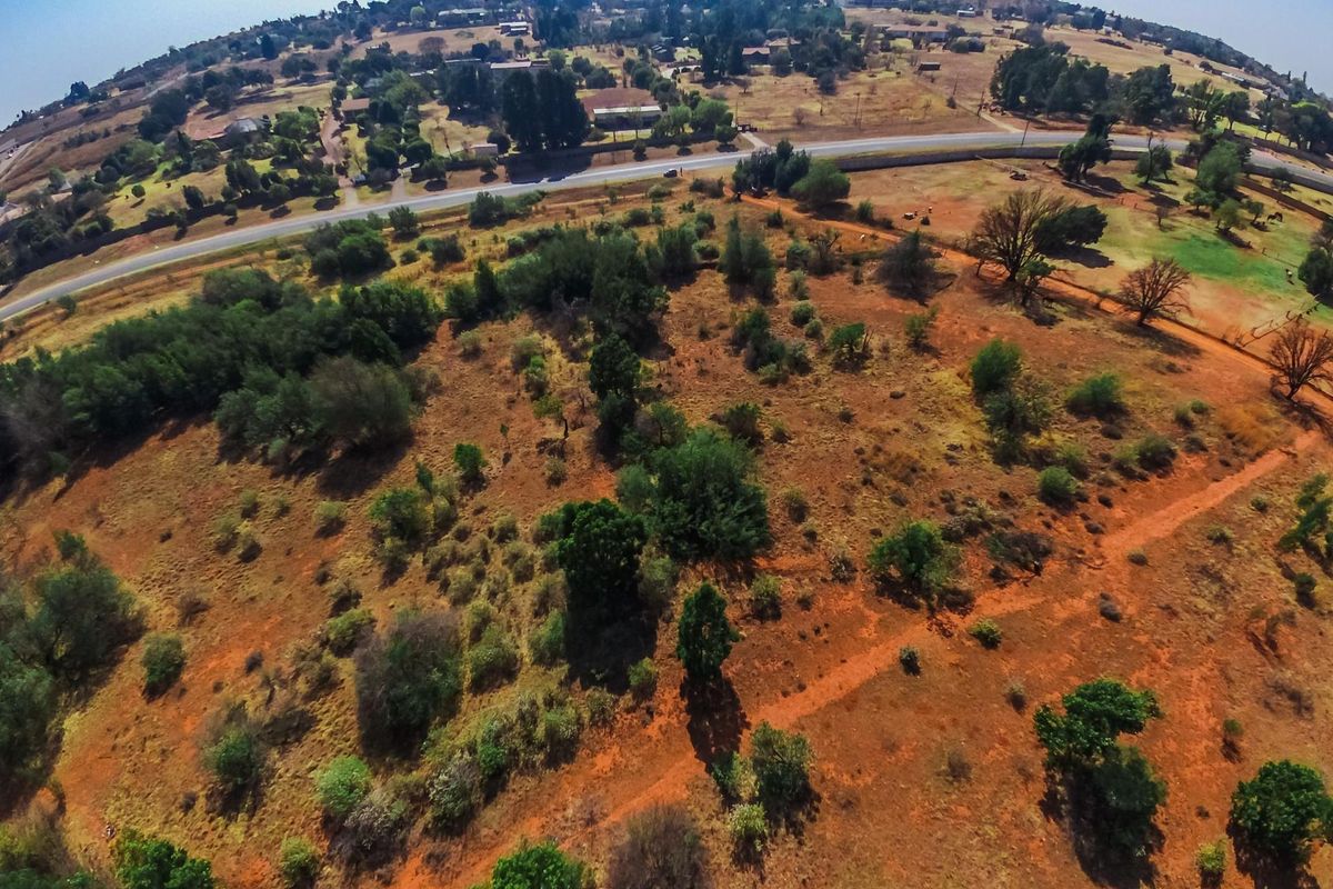 An aerial view of a large, undeveloped farm plot featuring natural vegetation, dirt paths, and surrounding rural landscape.