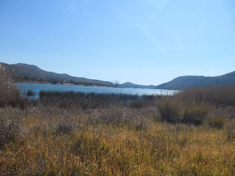 A scenic landscape view overlooking a natural lake or dam surrounded by hills and native vegetation.