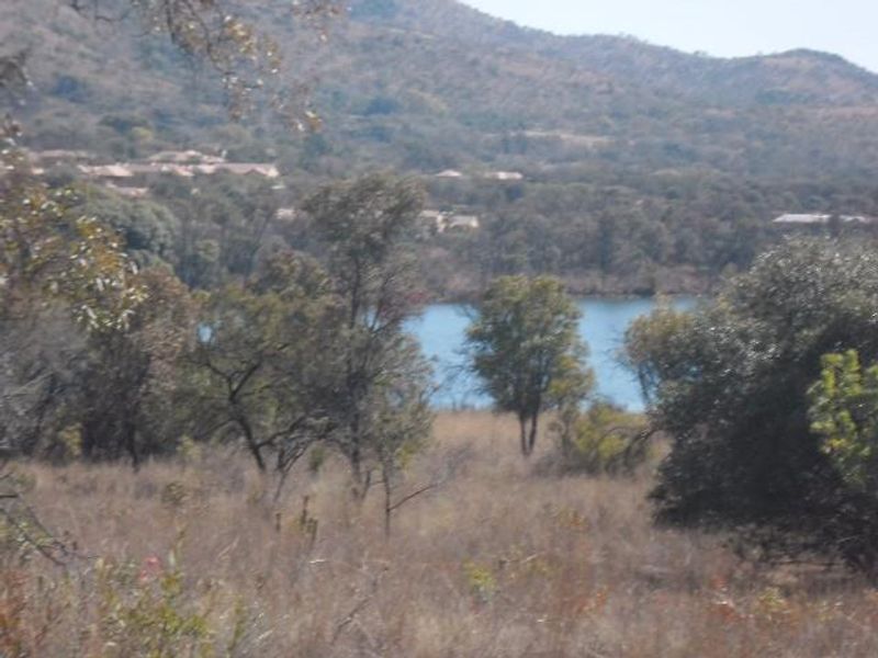 A scenic landscape view featuring natural vegetation, rolling hills, and a lake in the distance.