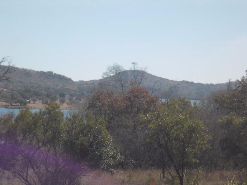 A scenic landscape view featuring rolling hills, native trees, and a glimpse of a nearby dam or lake.