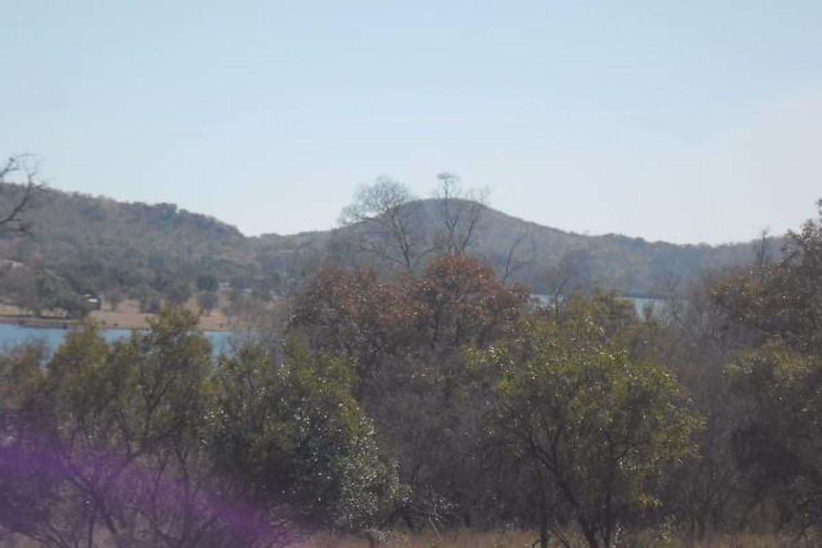 A scenic landscape view featuring rolling hills, native trees, and a glimpse of a nearby dam or lake.