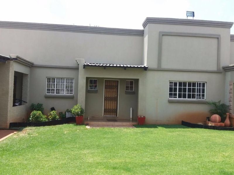 Front elevation of a small holding property featuring a covered carport, security gates, and a well-maintained lawn area.