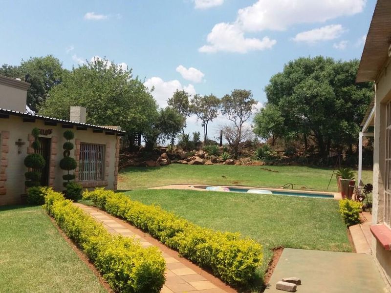 Rear view of the property featuring a well-maintained garden, a swimming pool, and a paved walkway connecting the building structures.