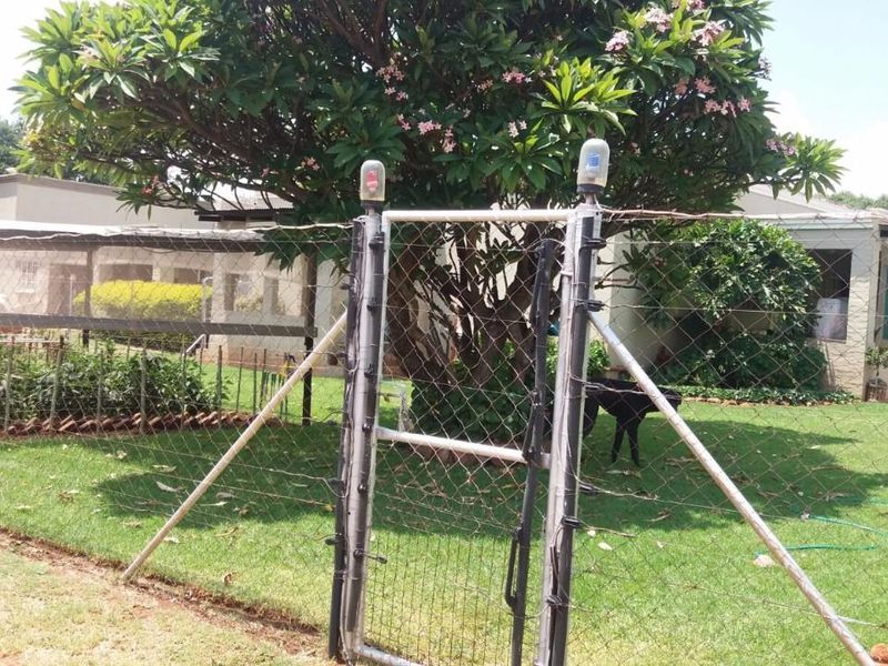 A garden area featuring a lawn, mature tree, and perimeter security fencing with an integrated gate.
