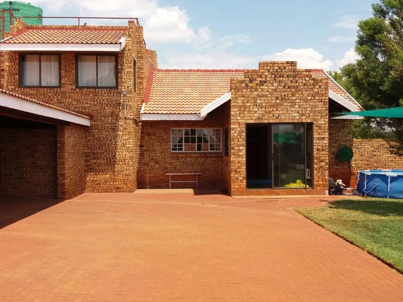 Rear view of a face-brick small holding property featuring a paved patio area, tiled roof, and established garden space.