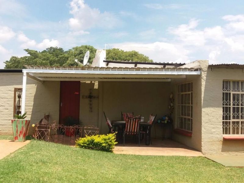A covered patio area adjacent to the garden and pool, featuring security bars on windows and a corrugated roof structure.
