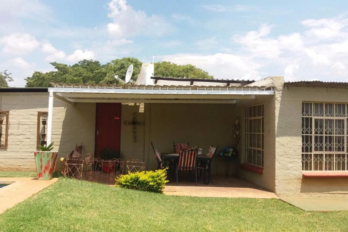 A covered patio area adjacent to the garden and pool, featuring security bars on windows and a corrugated roof structure.
