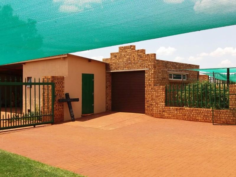 Front exterior view of the property featuring a paved driveway, face brick facade, secure metal gate, and overhead shade cloth canopy.
